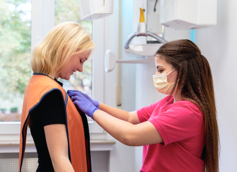 Zahnmedizinische Fachangestellte legt einer Patientin eine Röntgenschutzschürze an